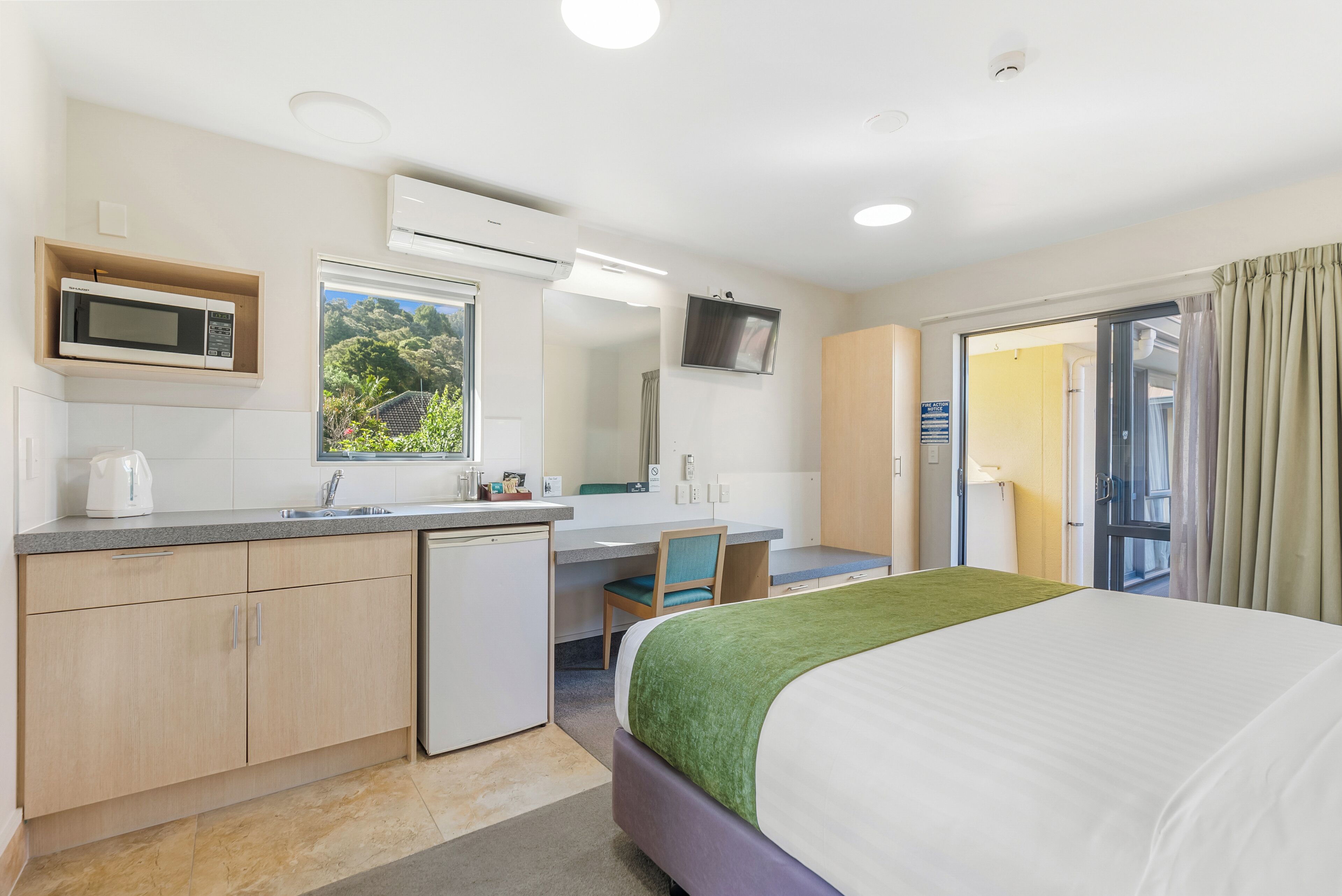 Una habitación de hotel con cama, escritorio, microondas, lavamanos y televisor.