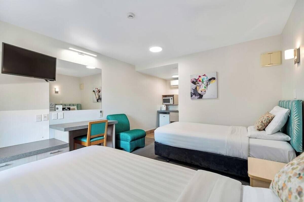 Habitación de hotel con dos camas, un escritorio, una silla, un televisor y un microondas.