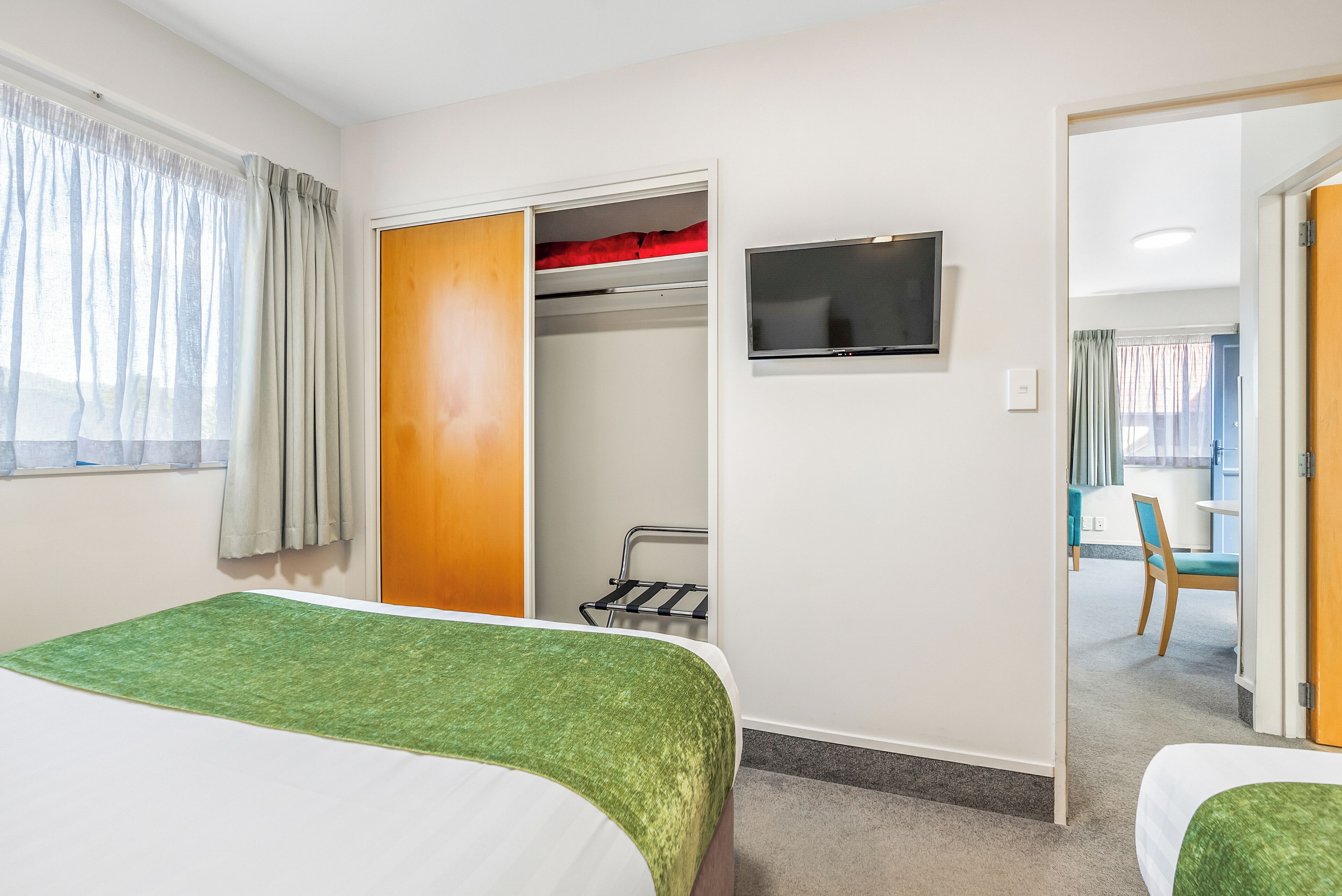 Habitación de hotel con cama, televisor, armario y vista a un comedor.