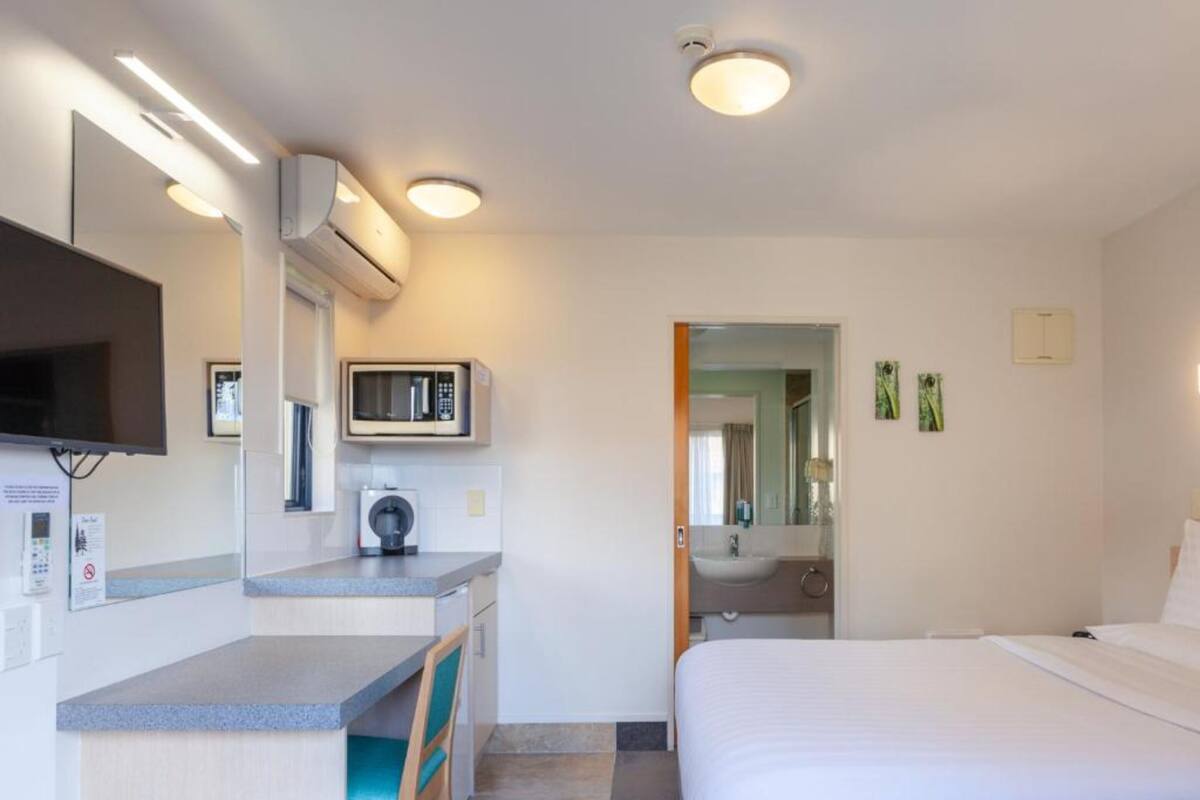 A hotel room with a bed, a desk, a chair, a microwave, a TV, and a bathroom visible through an open door.