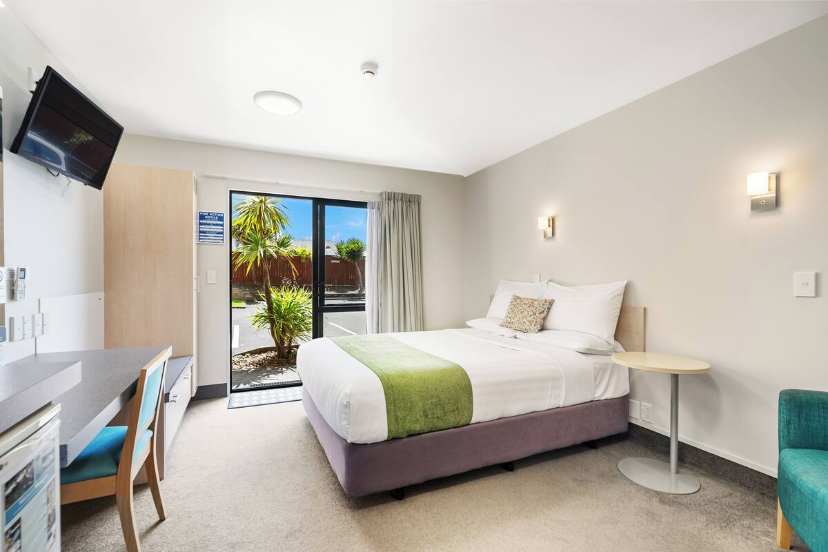 Habitación de hotel con cama, escritorio, silla, una mesita y televisor montado en la pared.