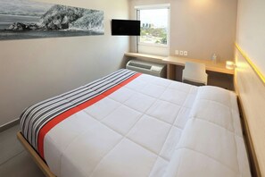A hotel room with a bed, a flat-screen TV mounted on the wall, a window with a view, a desk with a chair, and a heater. - City Express Junior by Marriott Cancun (Cancun)