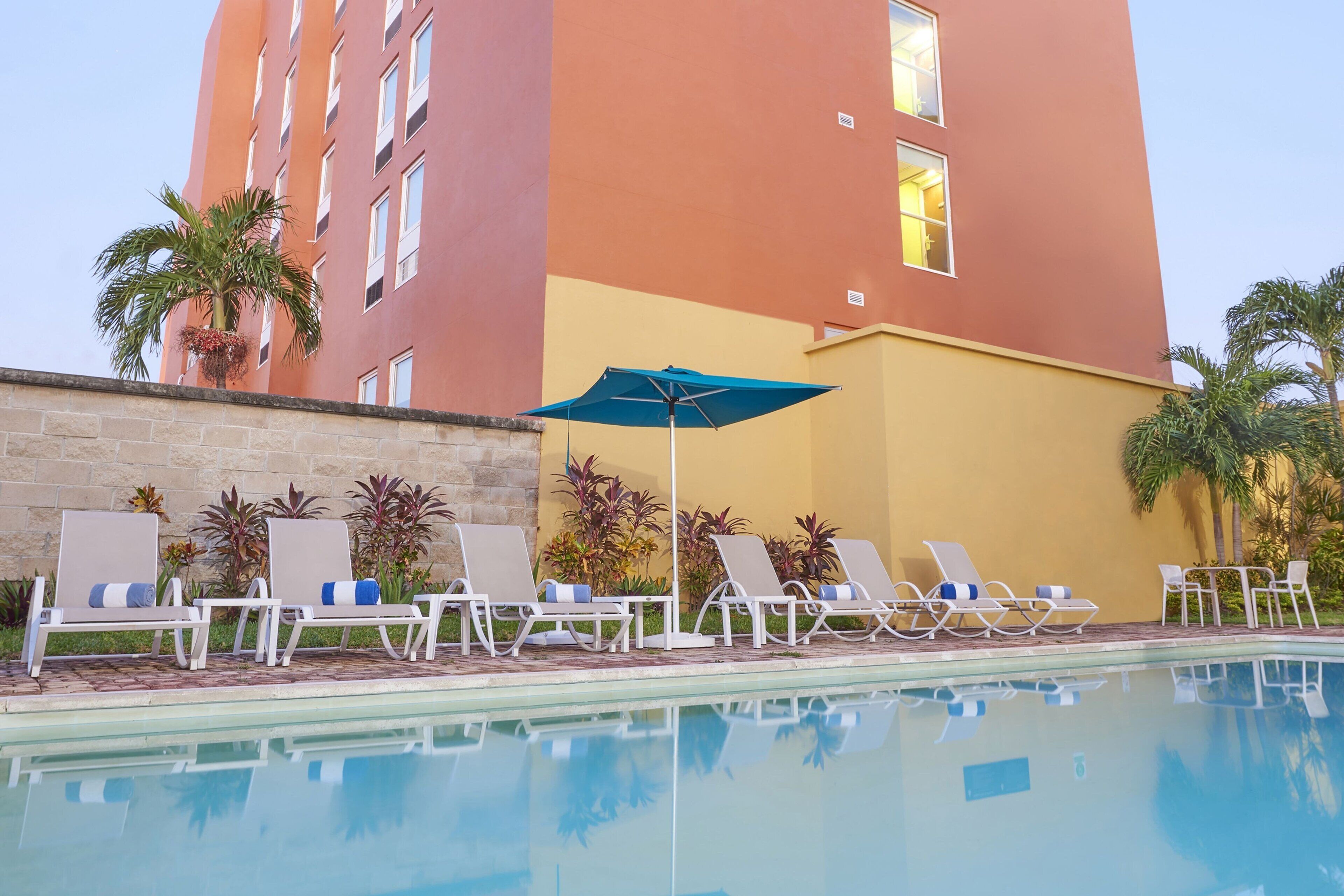 A poolside area with lounge chairs and an umbrella, surrounded by a building with a red and yellow facade.