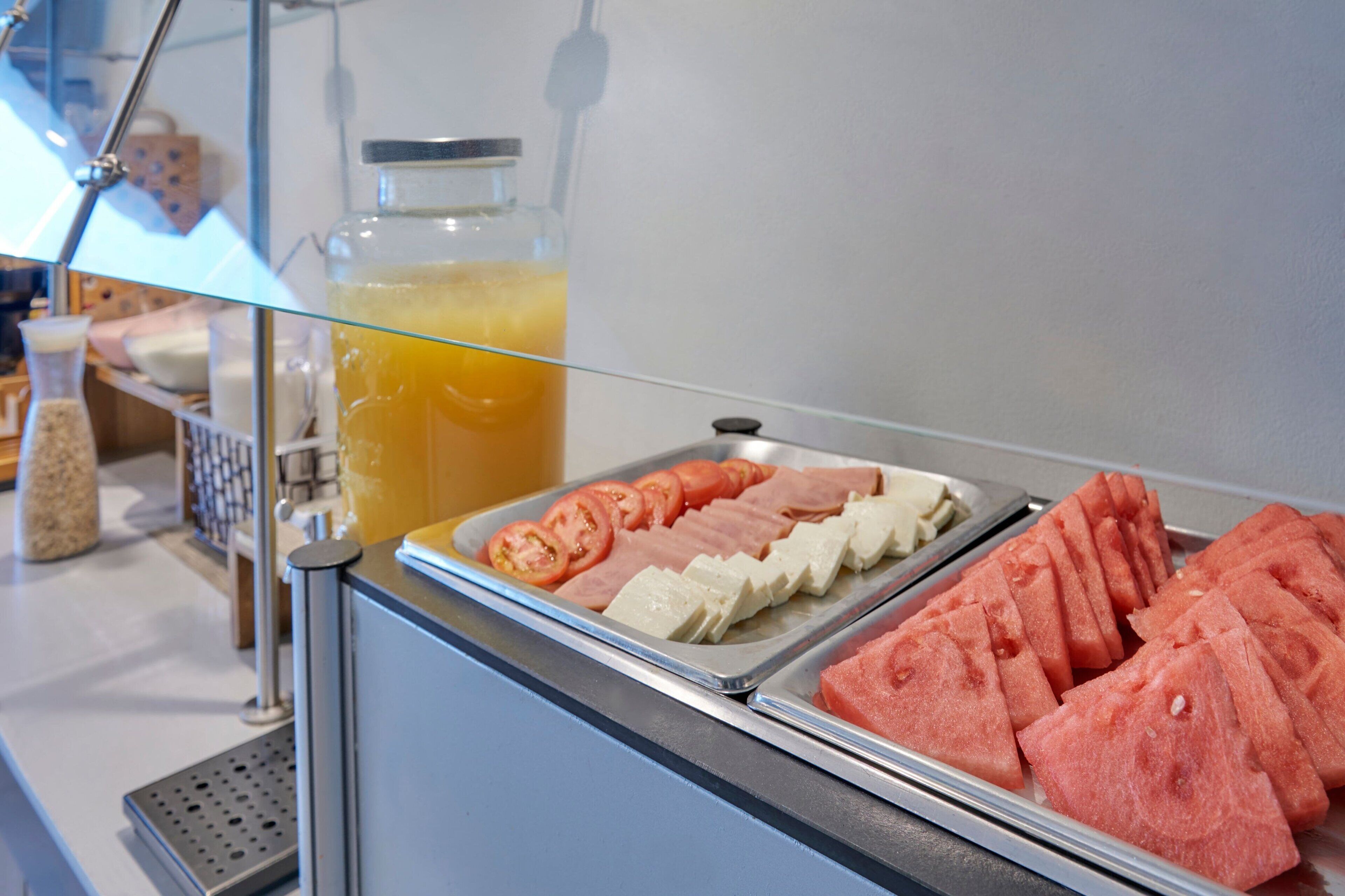 A buffet with sliced tomatoes, watermelon, and cheese.