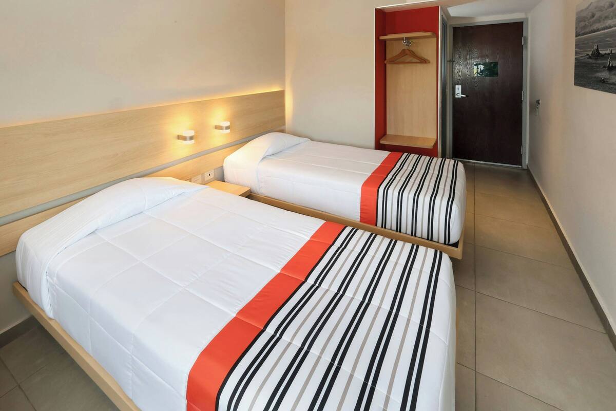 Hotellihuone, jossa on kaksi sänkyä, puinen pääty, vaatekaappi ja kuvalla koristeltu ovi.