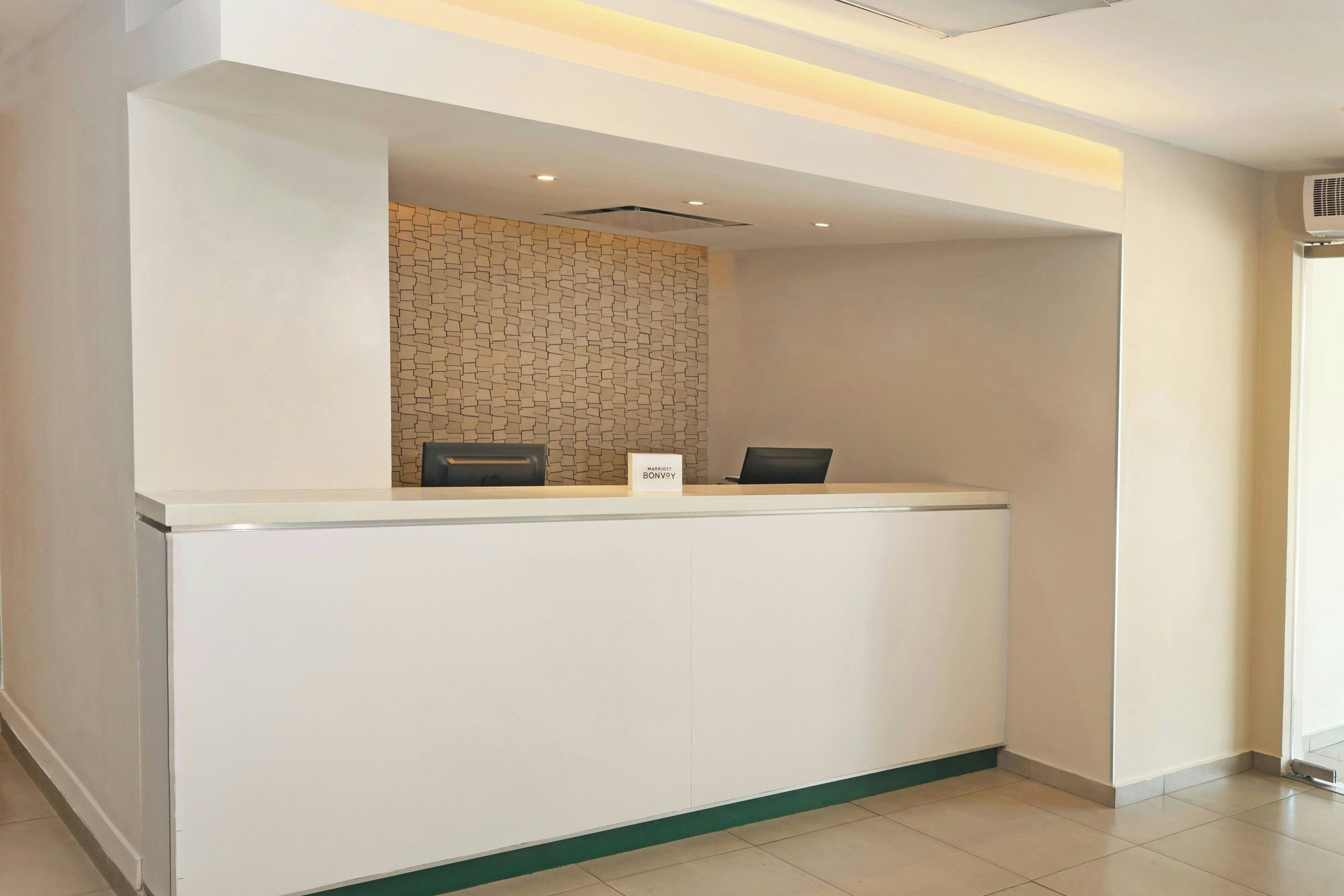 A reception desk with a nameplate, a small black object on the counter, and a patterned wall behind it.