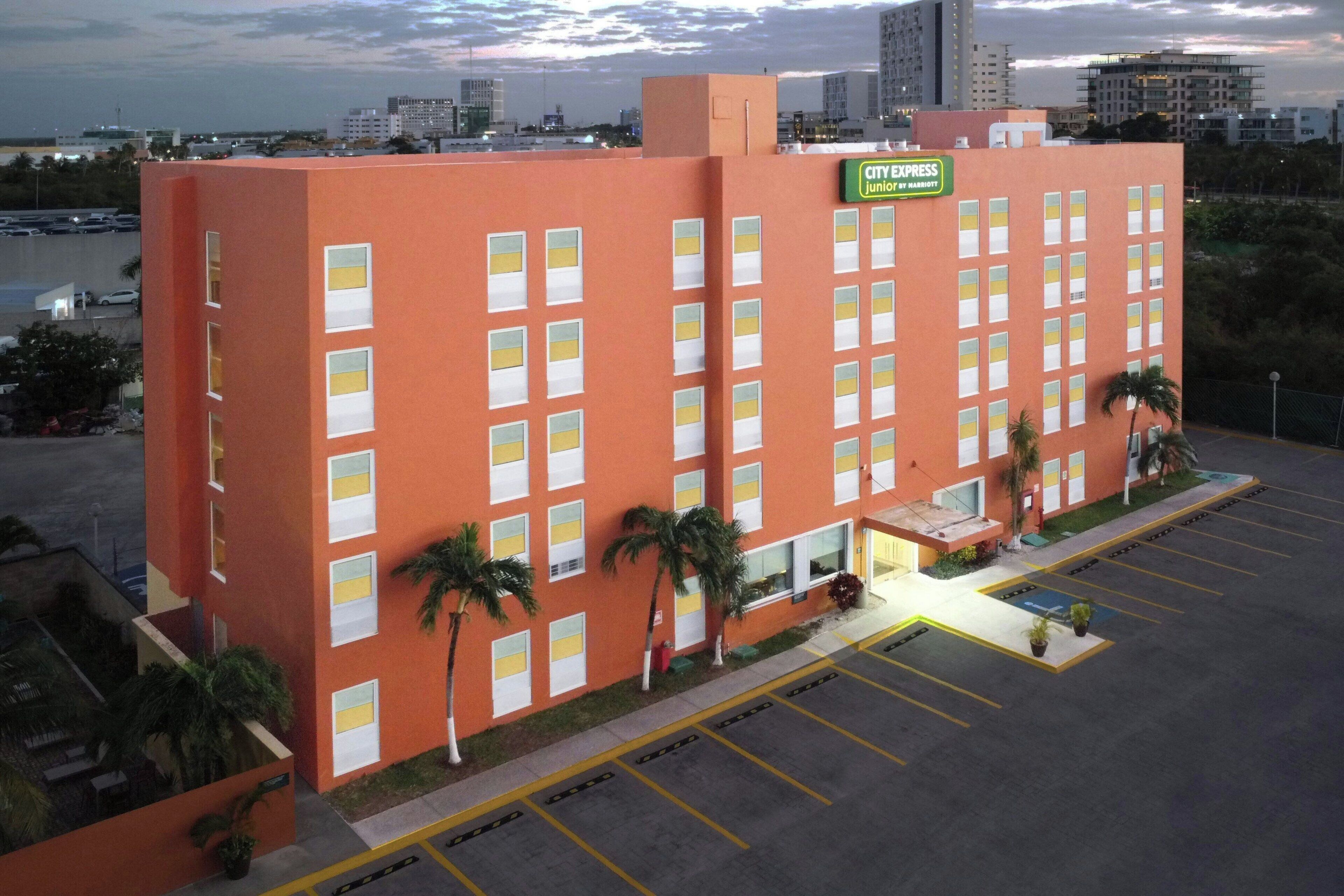 A multi-story hotel with a red facade, multiple windows, and a parking lot.