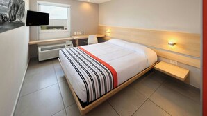 Una camera d'hotel moderna con un letto grande, una scrivania, una sedia, una televisione a schermo piatto montata a parete e una finestra con tende.