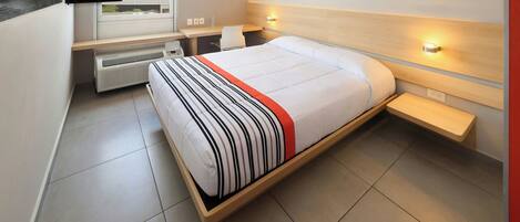 Una habitación de hotel moderna con una cama grande, un escritorio, una silla, un televisor de pantalla plana en la pared y una ventana con persianas.