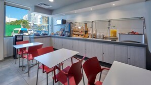 Un moderno caffè con tavoli bianchi e sedie rosse, una macchina da caffè e un bancone con diversi articoli.