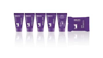 A row of purple skincare products including shampoo, conditioner, body wash, lotion, and a cleansing bar.