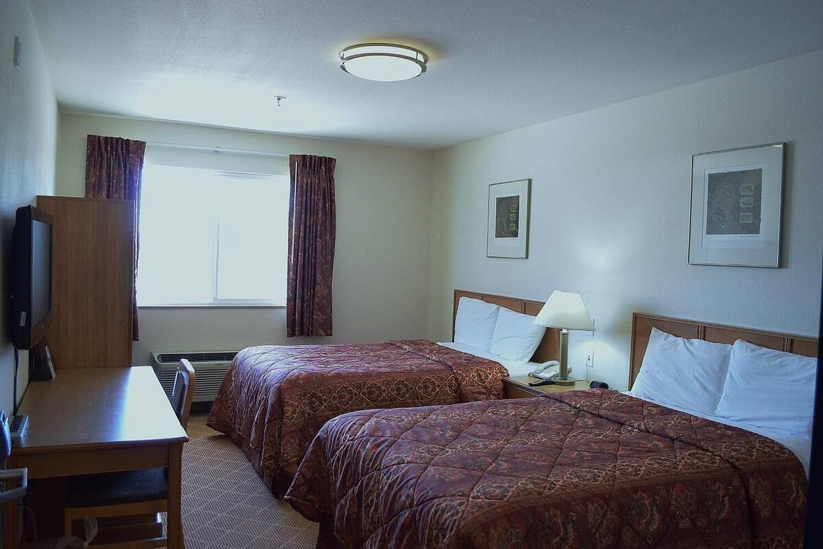 A hotel room with two beds, a desk, a chair, a TV, and a window with curtains.