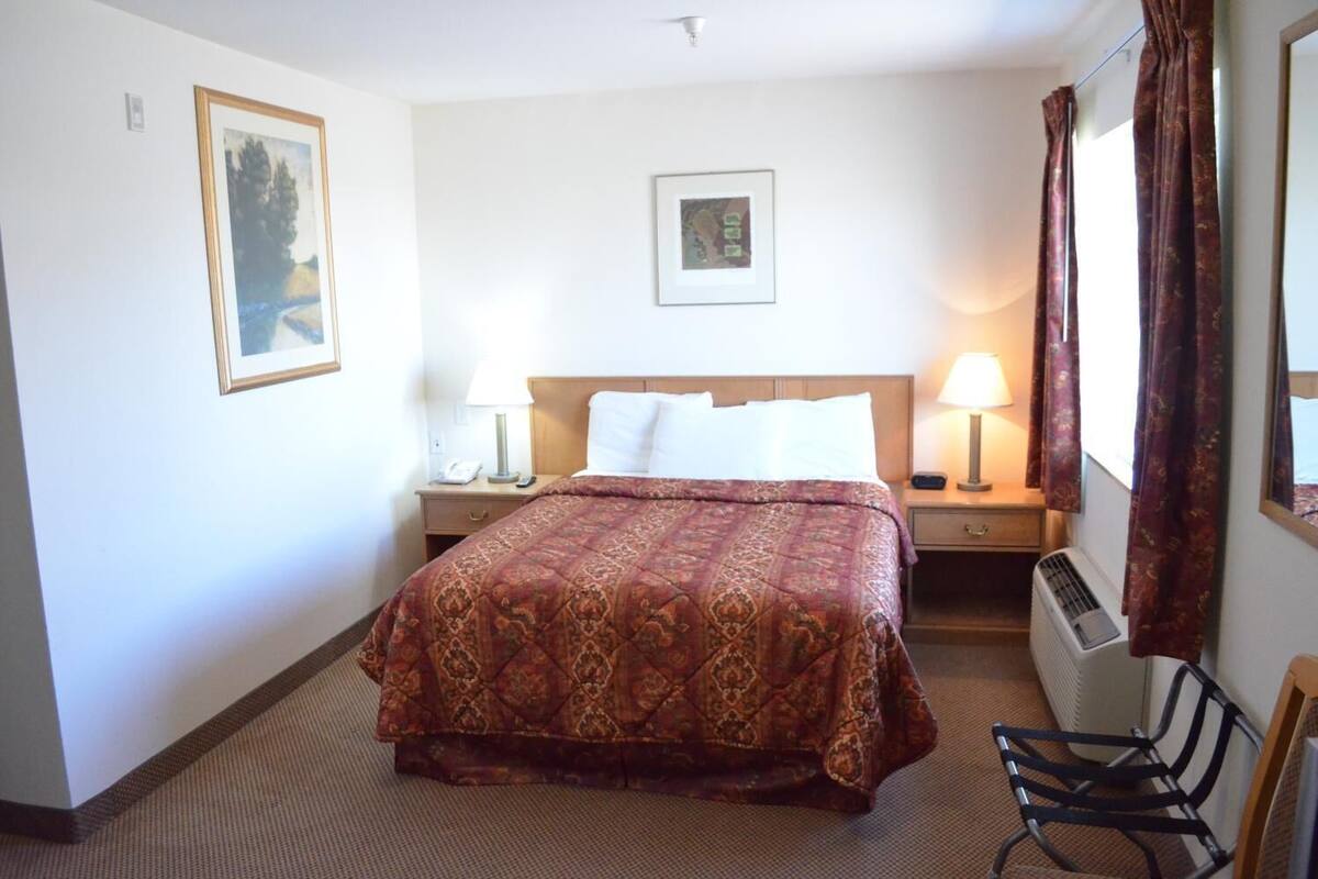 A hotel room with a large bed, two bedside tables with lamps, a chair, and a radiator.