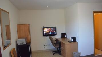 A small, clean room with a desk, chair, television, and a trash bin.