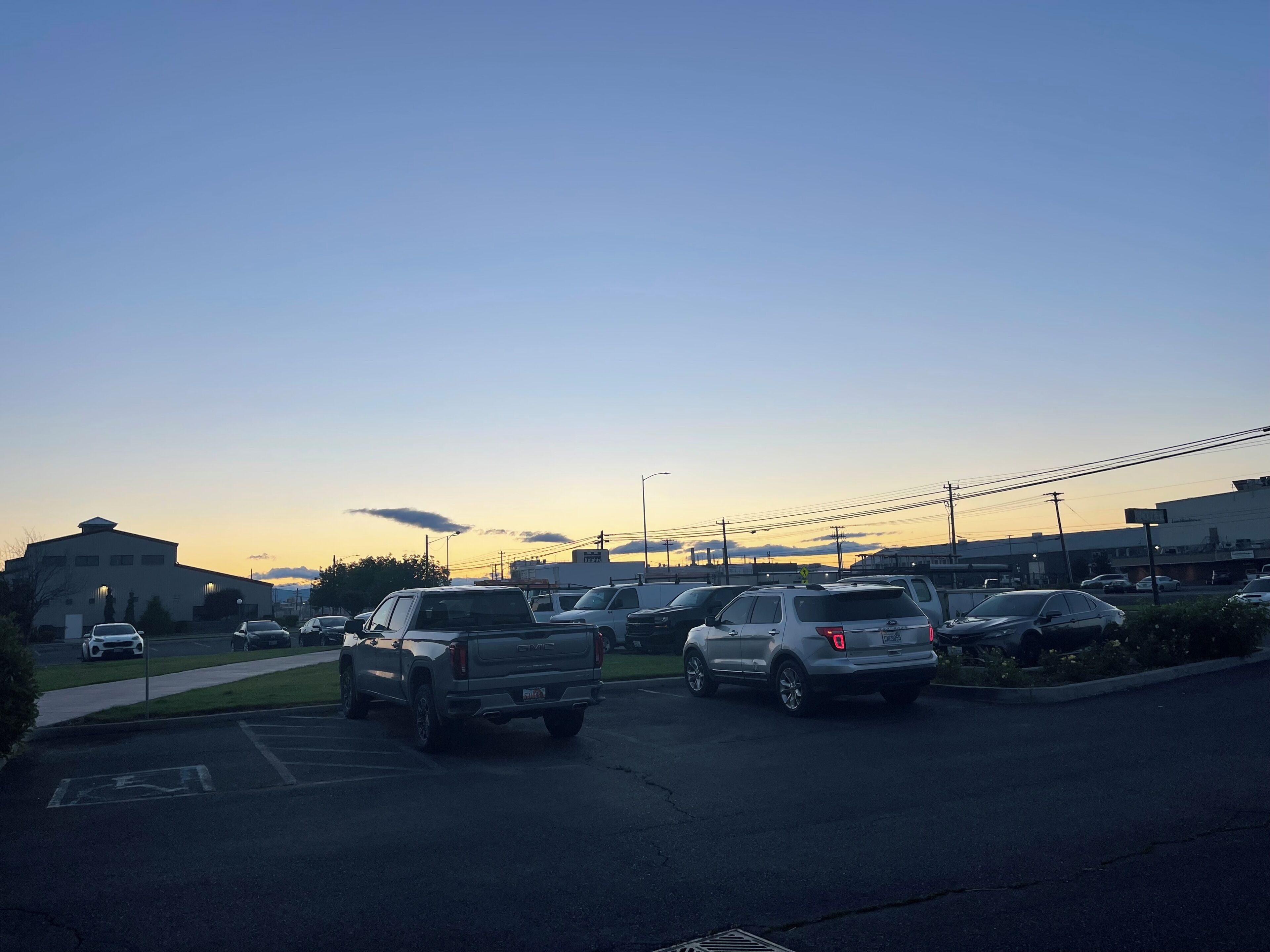 Un parking où sont stationnés plusieurs véhicules, dont un VUS blanc et une berline argentée, pendant la journée.