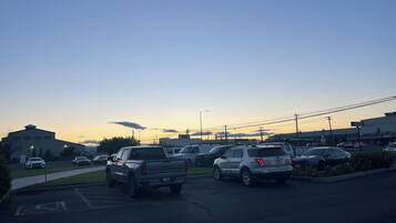 Un parking où sont stationnés plusieurs véhicules, dont un VUS blanc et une berline argentée, pendant la journée.