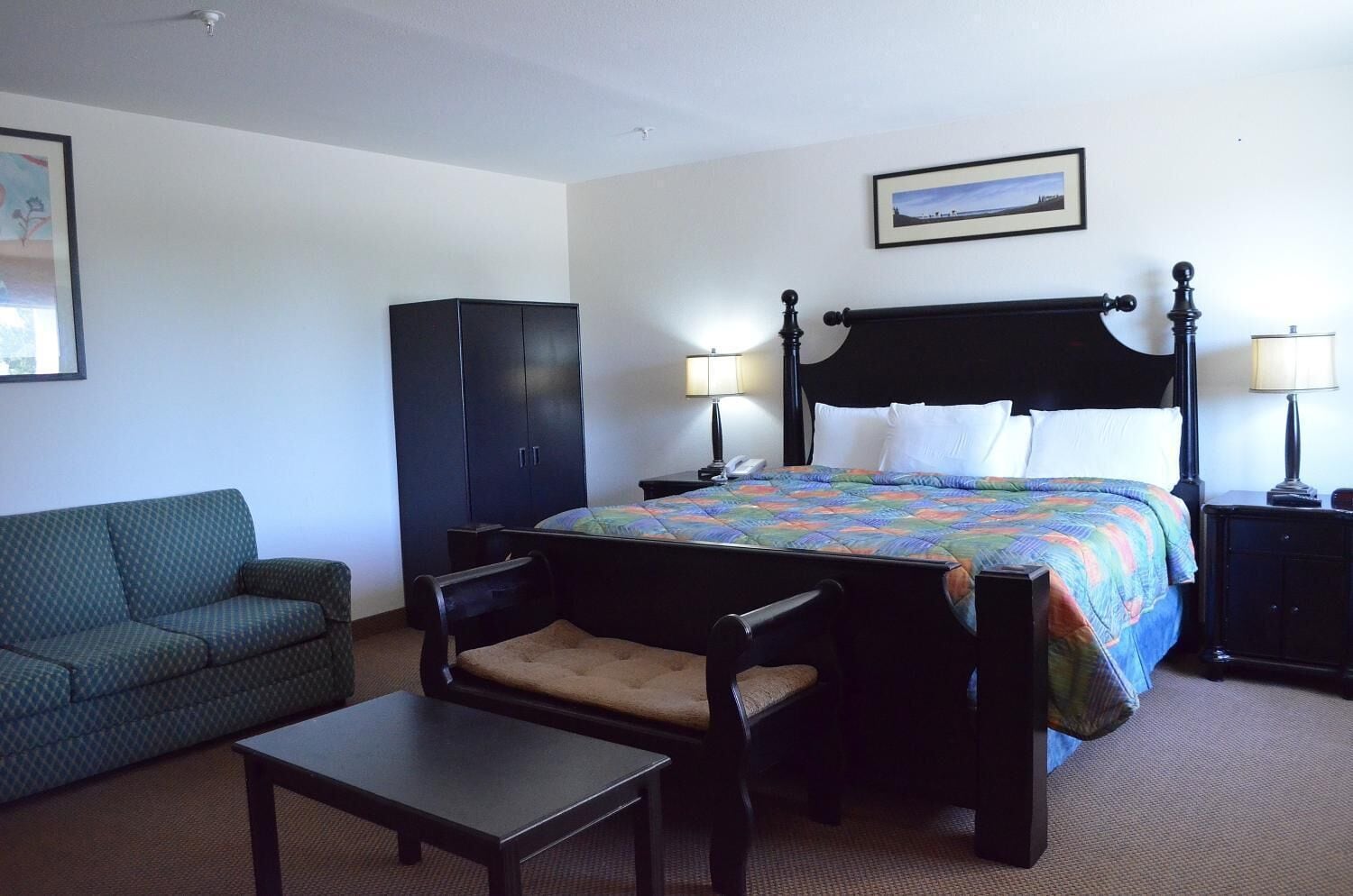 Een hotelkamer met een bed, een stoel, een klein tafeltje, een kledingkast en een schilderij aan de muur.