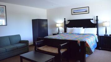 Een hotelkamer met een bed, een stoel, een klein tafeltje, een kledingkast en een schilderij aan de muur.