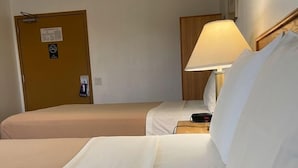Une chambre d’hôtel avec deux lits, une table de chevet avec une lampe, une tête de lit en bois et une porte avec une pancarte.