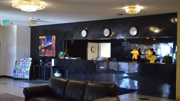 Un hall d’entrée avec un comptoir de réception noir, plusieurs horloges, un canapé en cuir noir et un grand tableau accroché au mur.