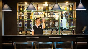 A bar area with a bartender, shelves of liquor bottles, and a 'CAFE' sign. - Holidays-hanoi Hotel (Hanoi)