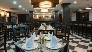 A restaurant with checkered flooring, round tables with white napkins, and pendant lighting. - Holidays-hanoi Hotel (Hanoi)