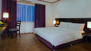 A hotel room with a large bed, a desk with a chair, and a window with purple curtains. - Holidays-hanoi Hotel (Hanoi)