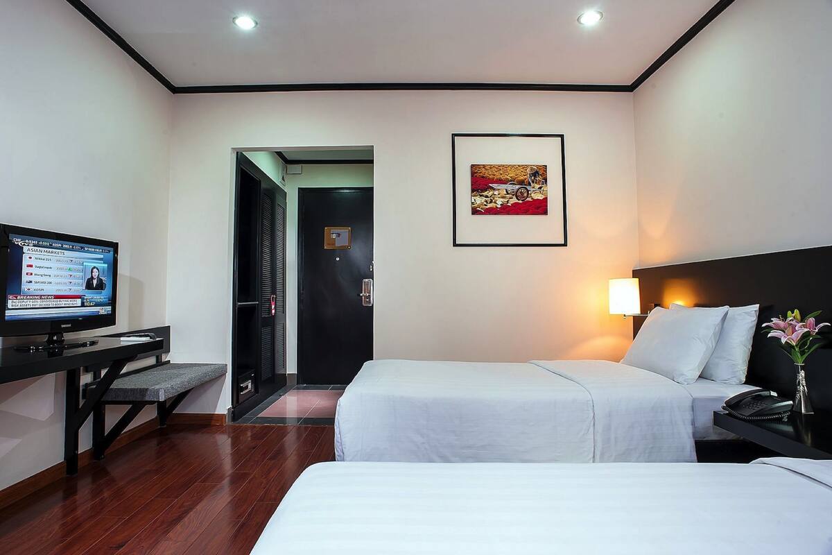 Habitación de hotel con dos camas, un escritorio con computadora, televisión y un cuadro en la pared.