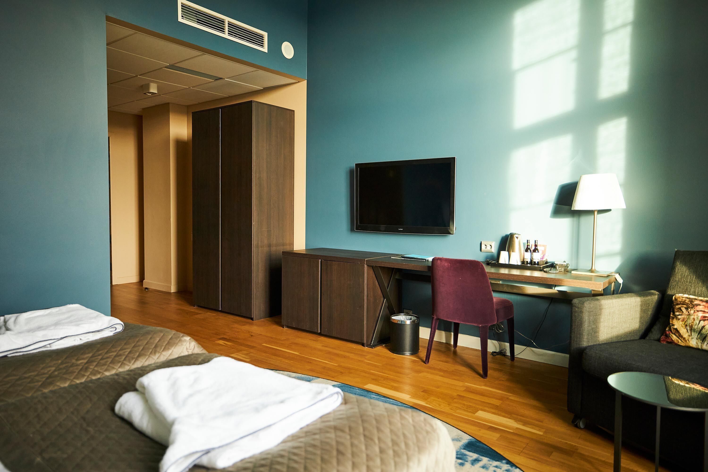 Una camera d'albergo con due letti, una scrivania, una sedia, una TV e una lampada.