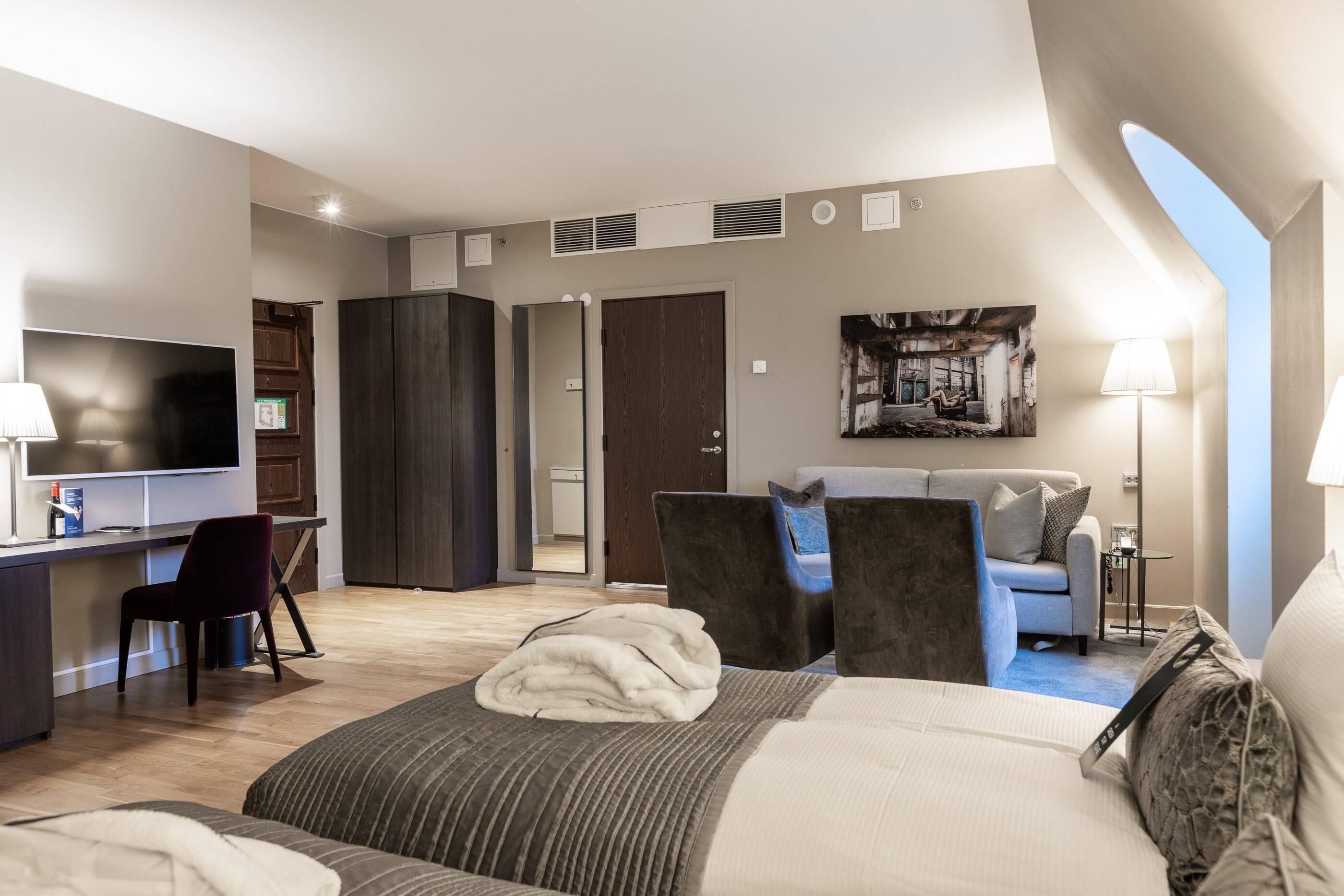 A modern hotel room with a bed, desk, and seating area.