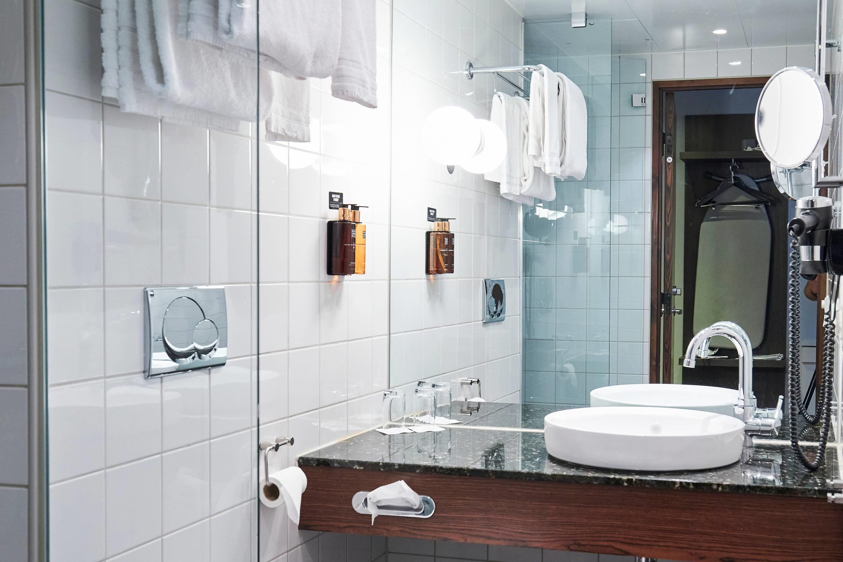 A modern bathroom with two sinks, a large mirror, and a towel rack.