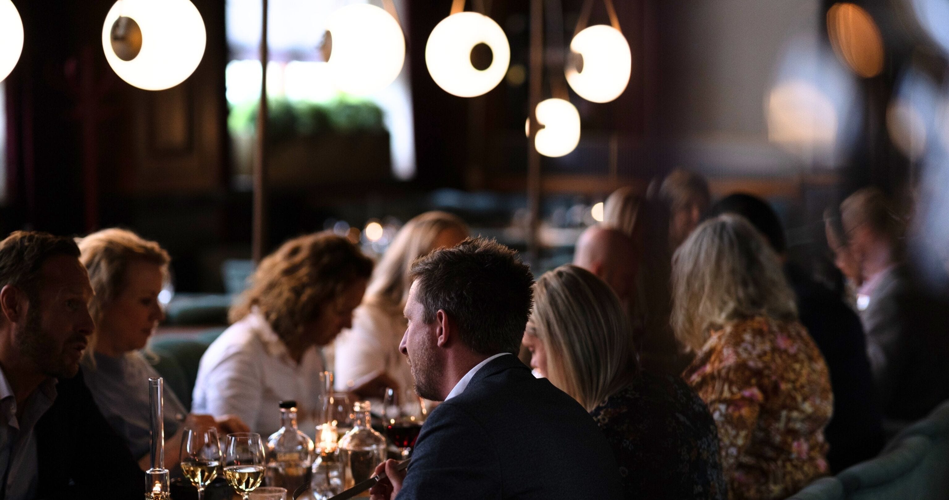 Un grupo de personas cenando en un restaurante con ambiente tenue y lámparas colgantes.