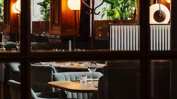 L’intérieur d’un restaurant, avec des tables dressées pour le service, des chaises et une vue sur l’extérieur grâce à de grandes fenêtres.