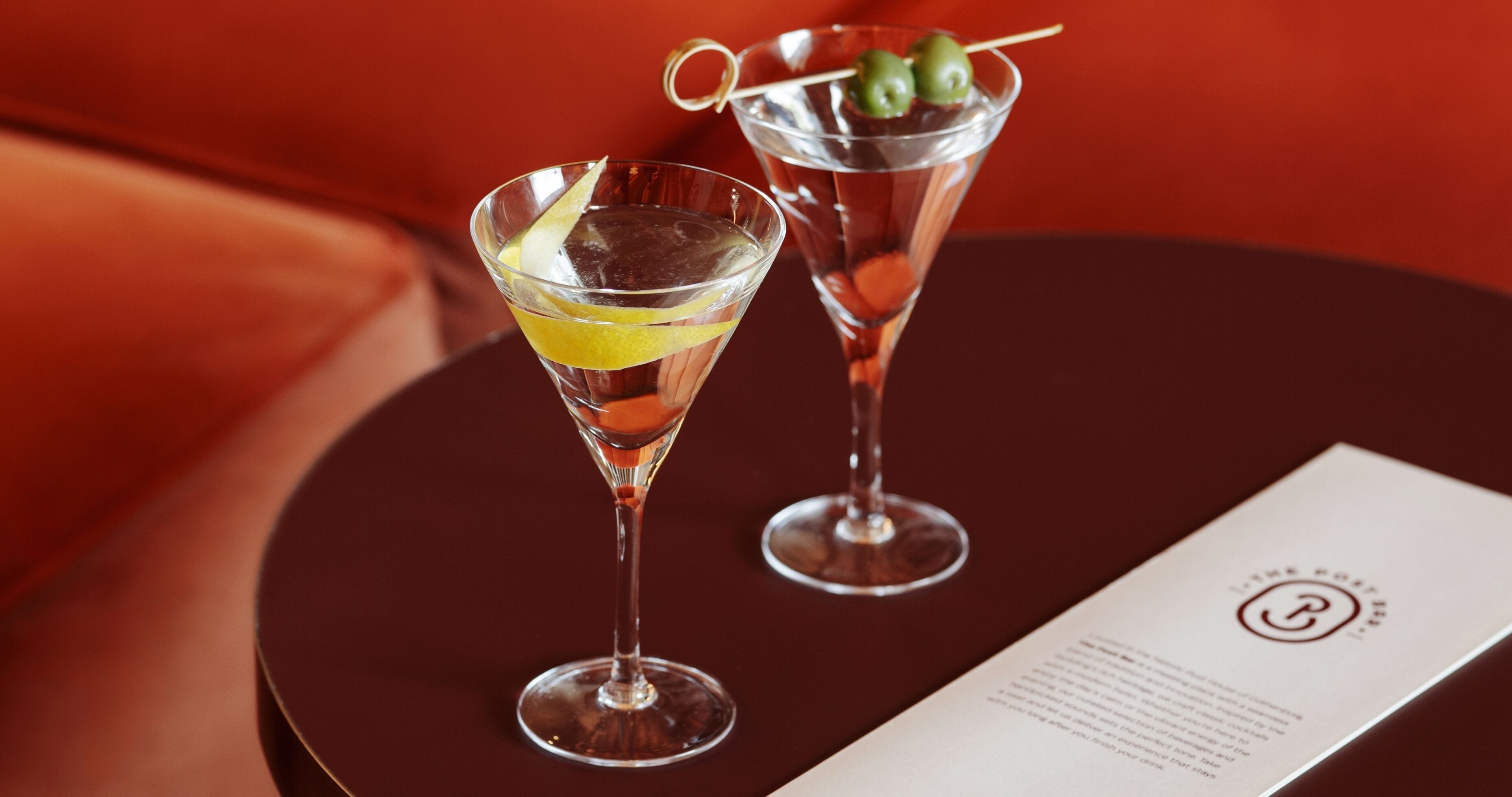 Zwei Martini-Gläser mit Garnitur auf einem runden Tisch mit einer Speisekarte.