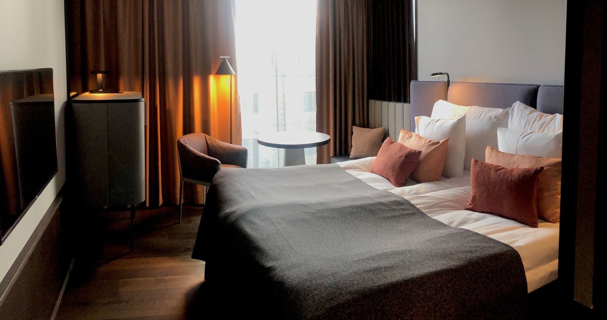 A hotel room with a bed, a chair, a small table, and a lamp.