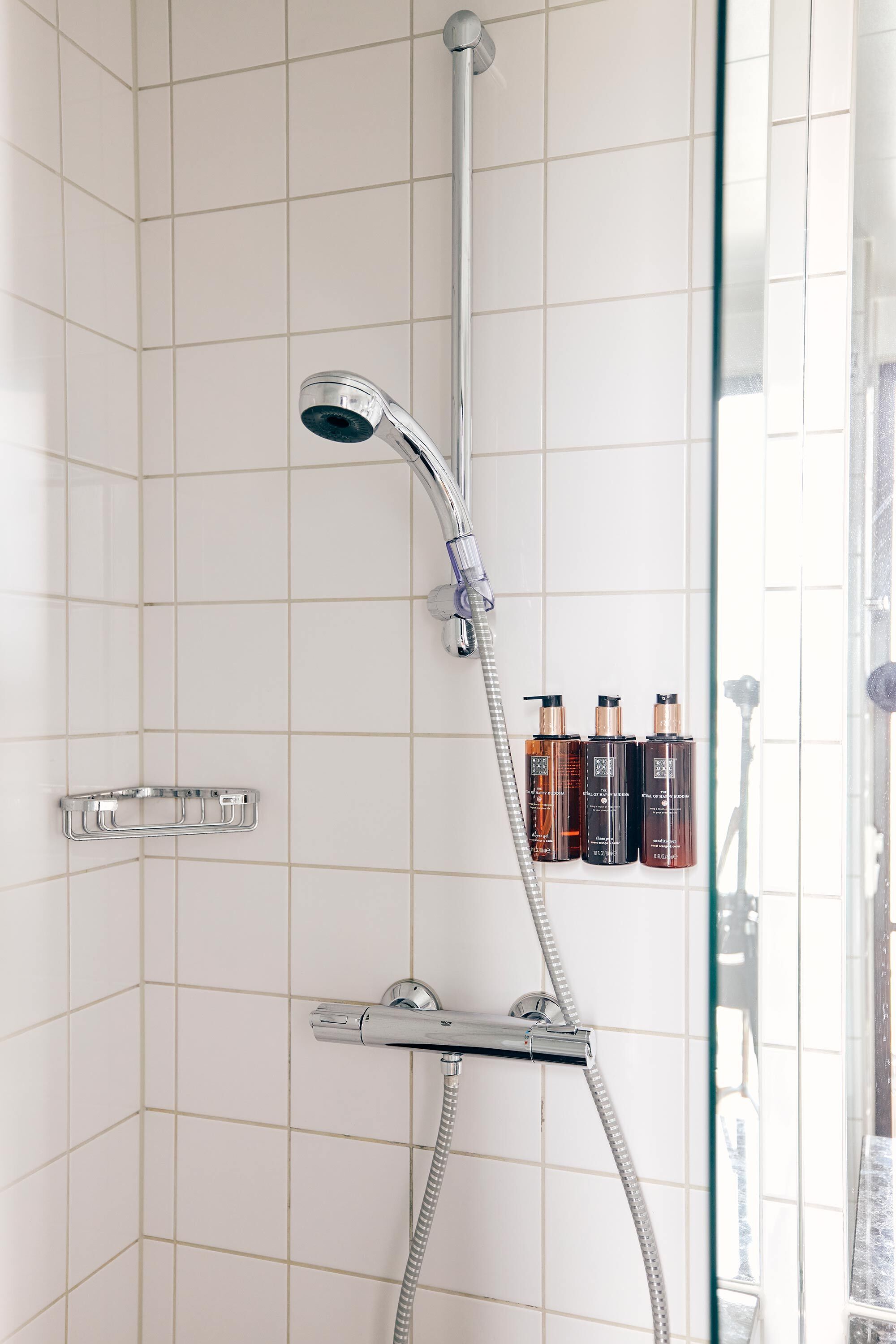 Eine Dusche mit Duschbrause, Wandarmatur, einer Duschkabine aus Glas und Ablage für Toilettenartikel.