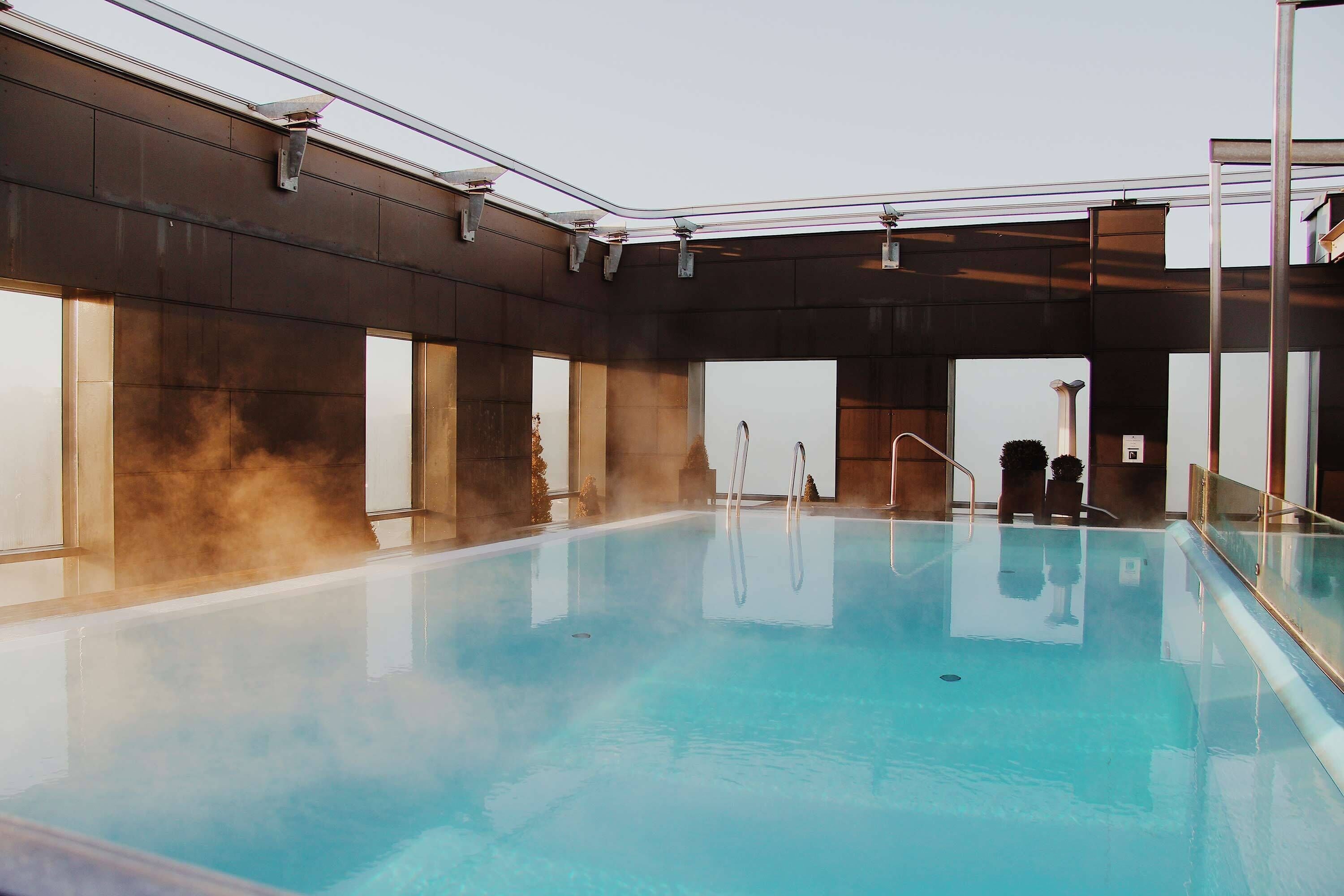Una piscina interior con agua cristalina, rodeada de paredes con amplias ventanas y un diseño moderno.