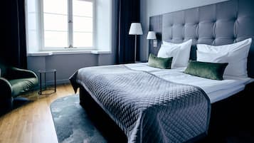 Ett hotellrum med en stor säng, ett nattduksbord, en lampa och utsikt över omgivningarna genom ett fönster.