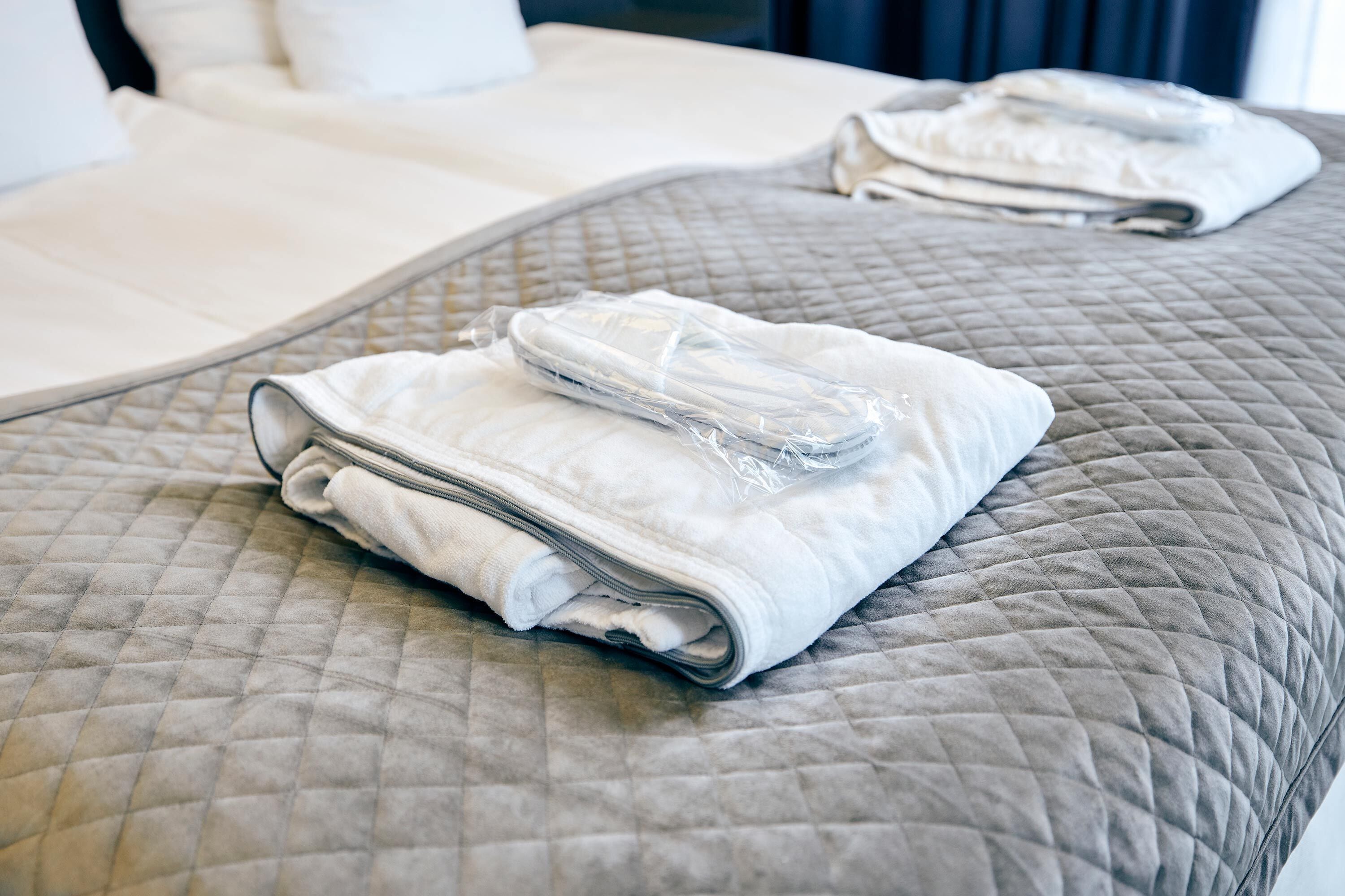 A neatly made bed with a quilted gray bedspread and folded white towels.