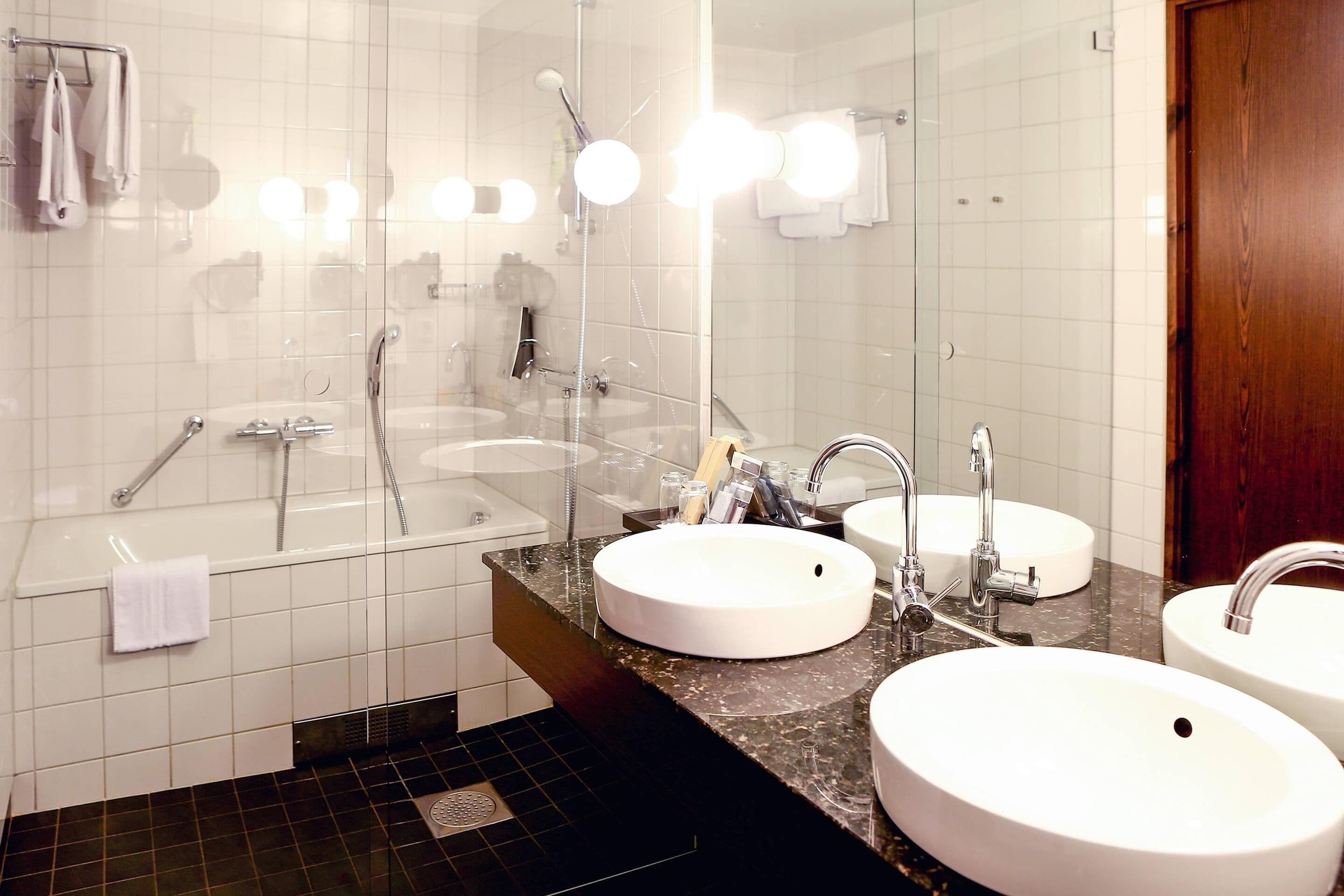A modern bathroom with a bathtub, two sinks, and a large mirror.