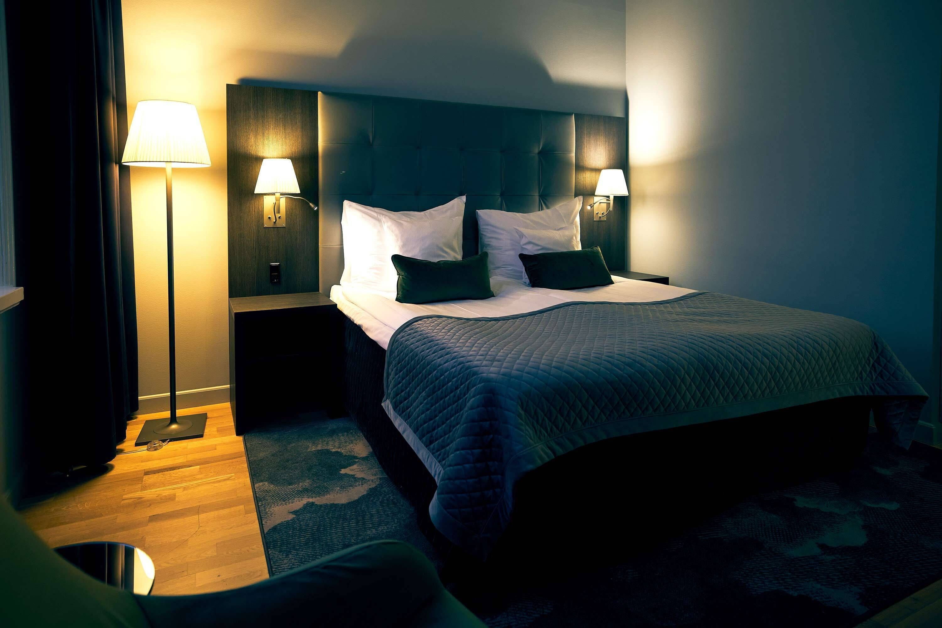 A hotel room with a large bed, two bedside lamps, and a wooden floor.