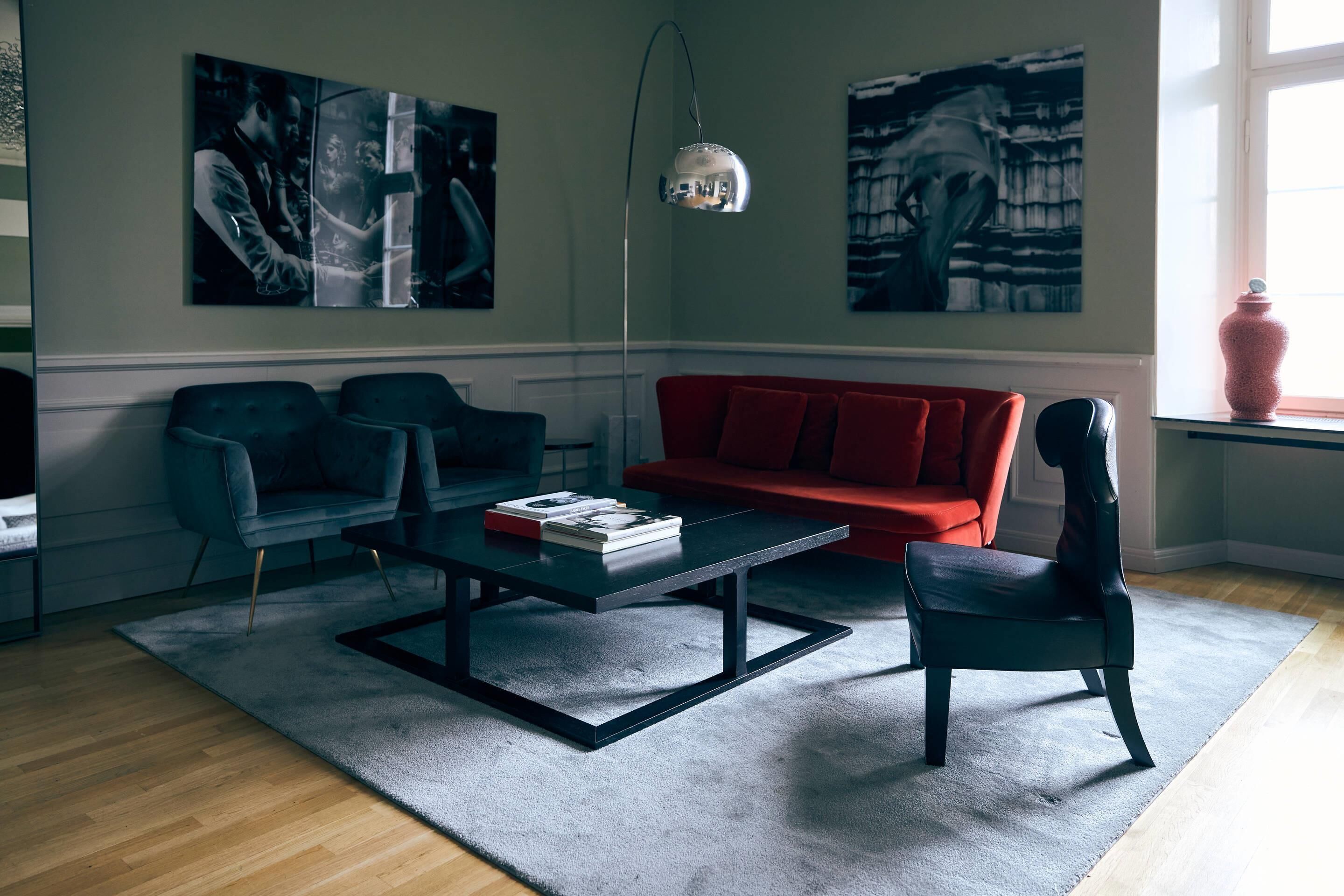 Una sala de estar con un sofá rojo, dos sillones, una mesa de centro y arte abstracto en las paredes.