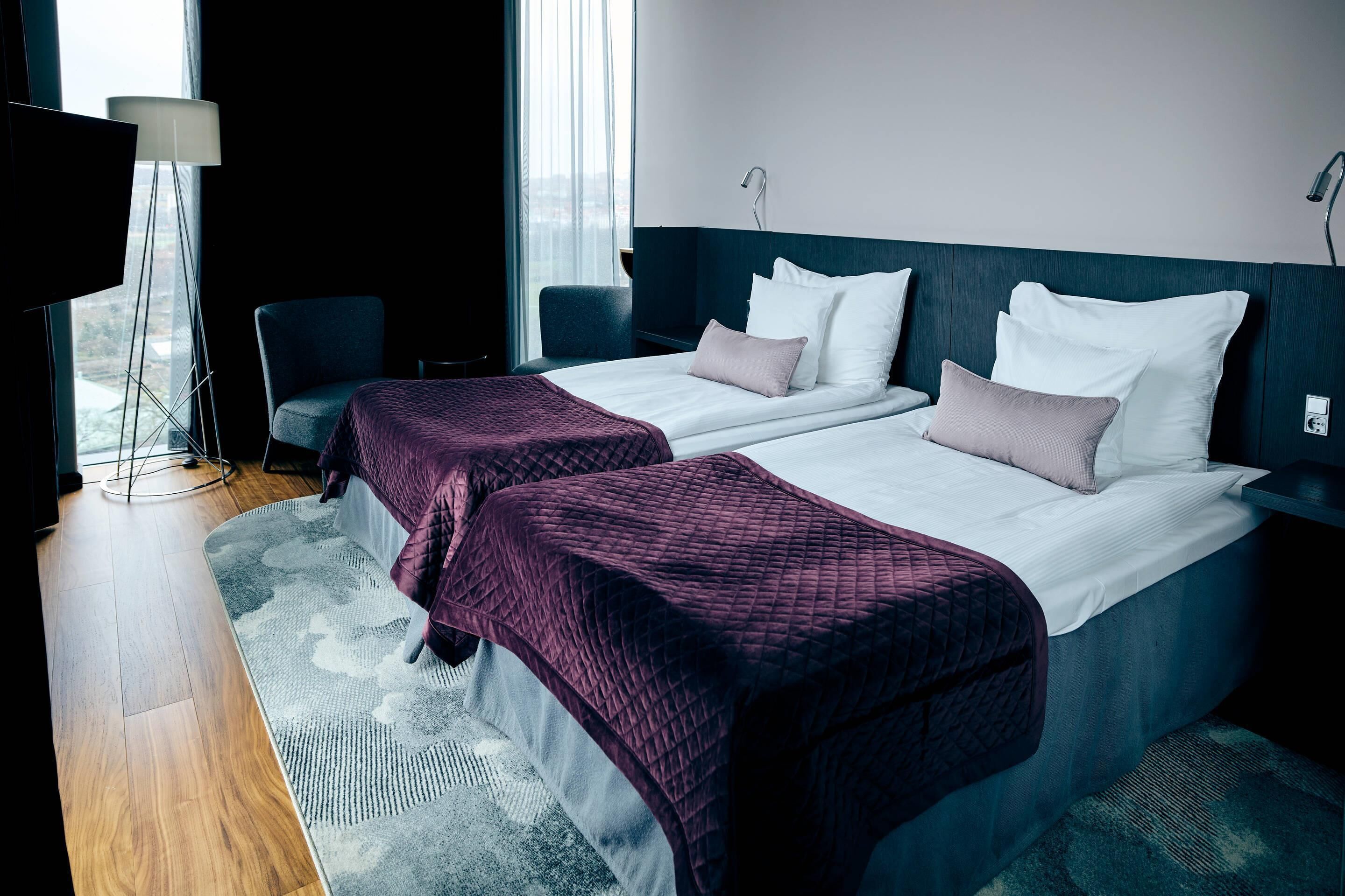 A hotel room with two beds, a desk, a chair, and a large window.