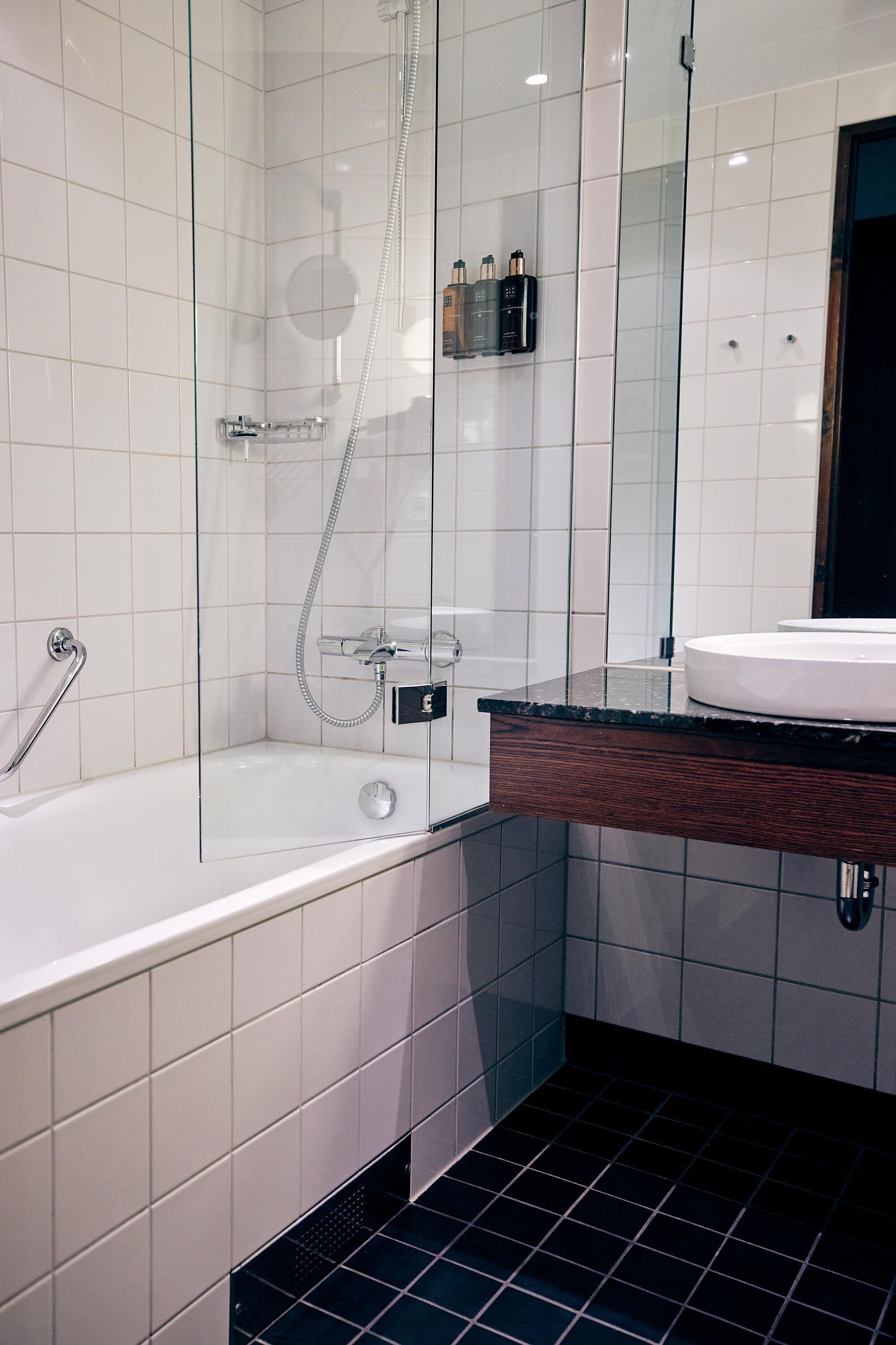 A modern bathroom with a glass-enclosed shower, a white bathtub, and a wooden vanity with a sink.