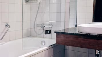 A modern bathroom with a glass-enclosed shower, a white bathtub, and a wooden vanity with a sink.