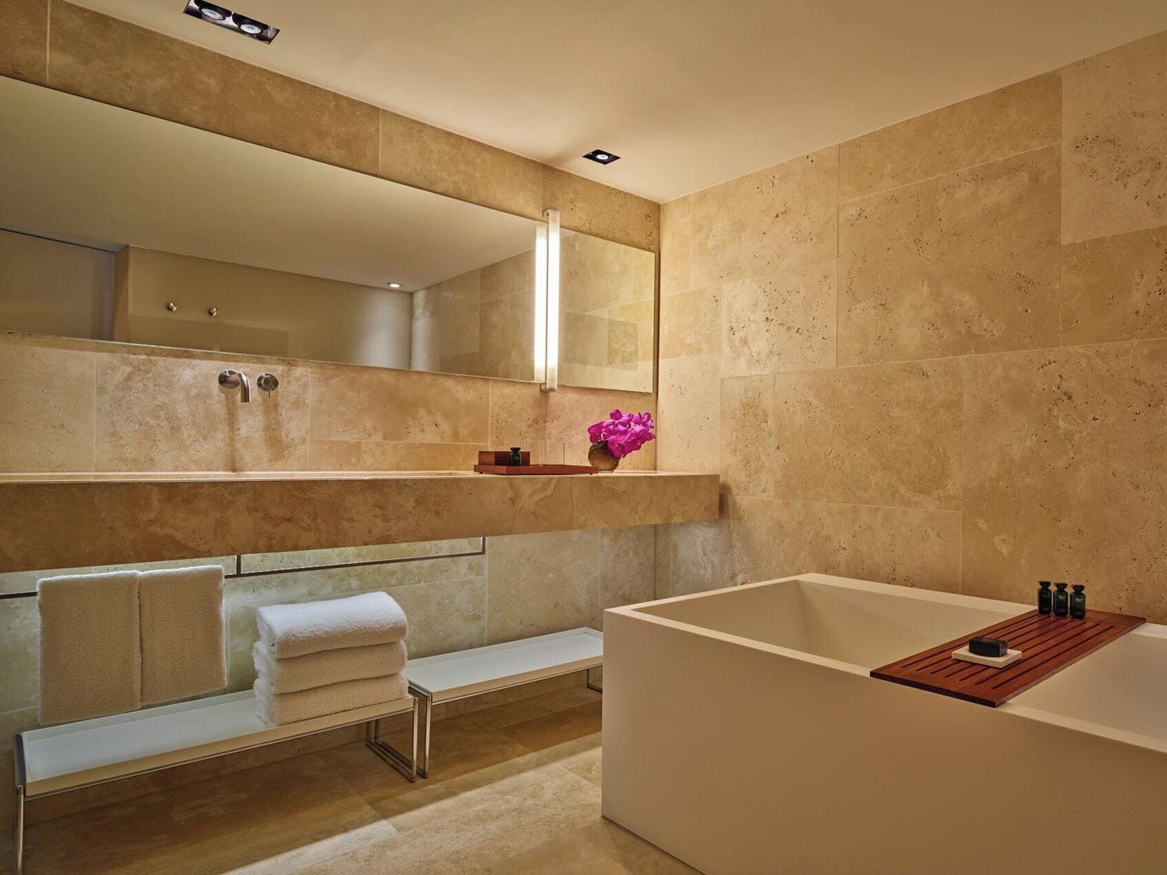 A modern bathroom with a large bathtub, a bench, and a mirror above the sink.