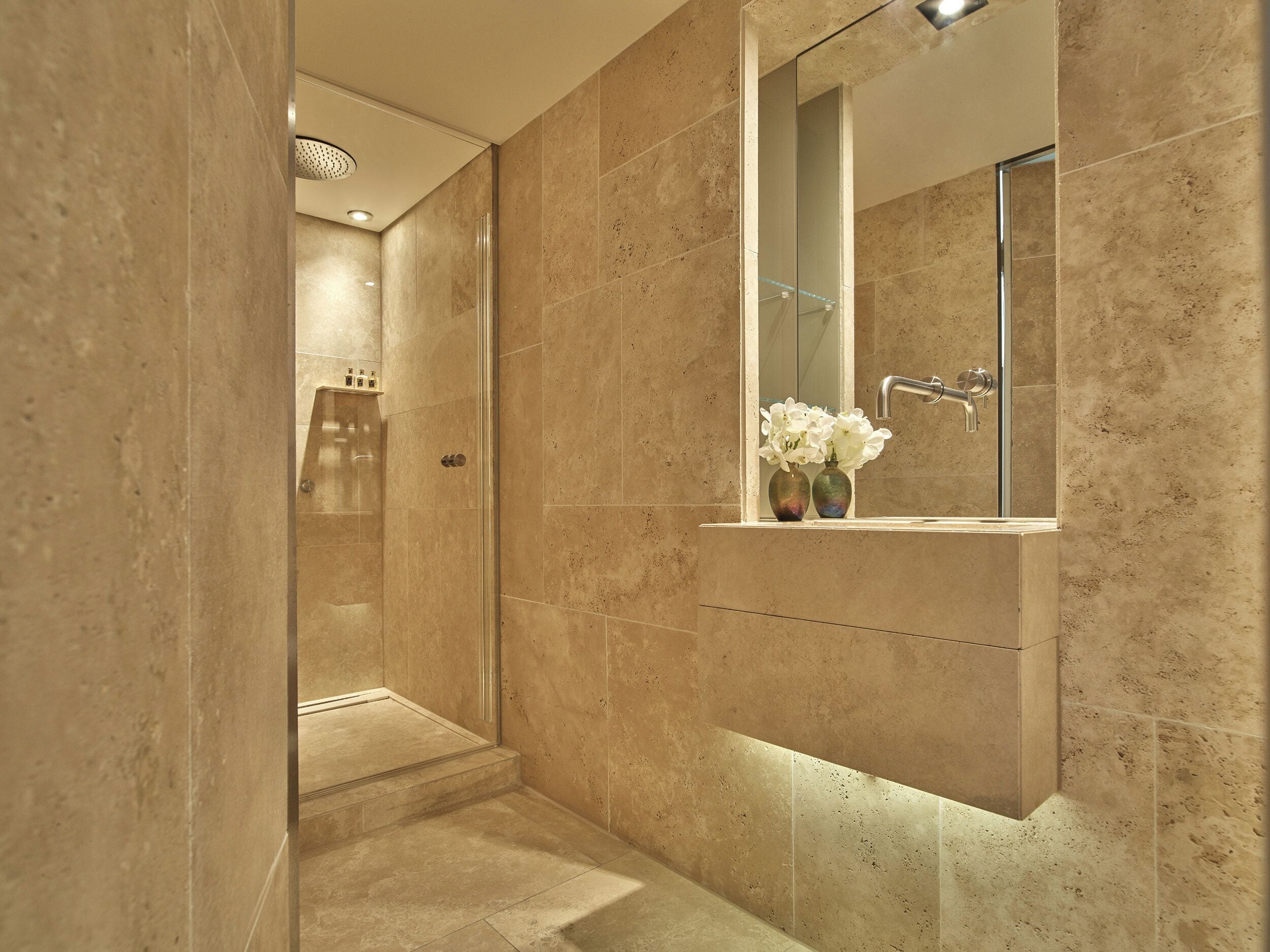 A modern bathroom with a glass-enclosed shower, a vanity with a mirror, and a vase with flowers.