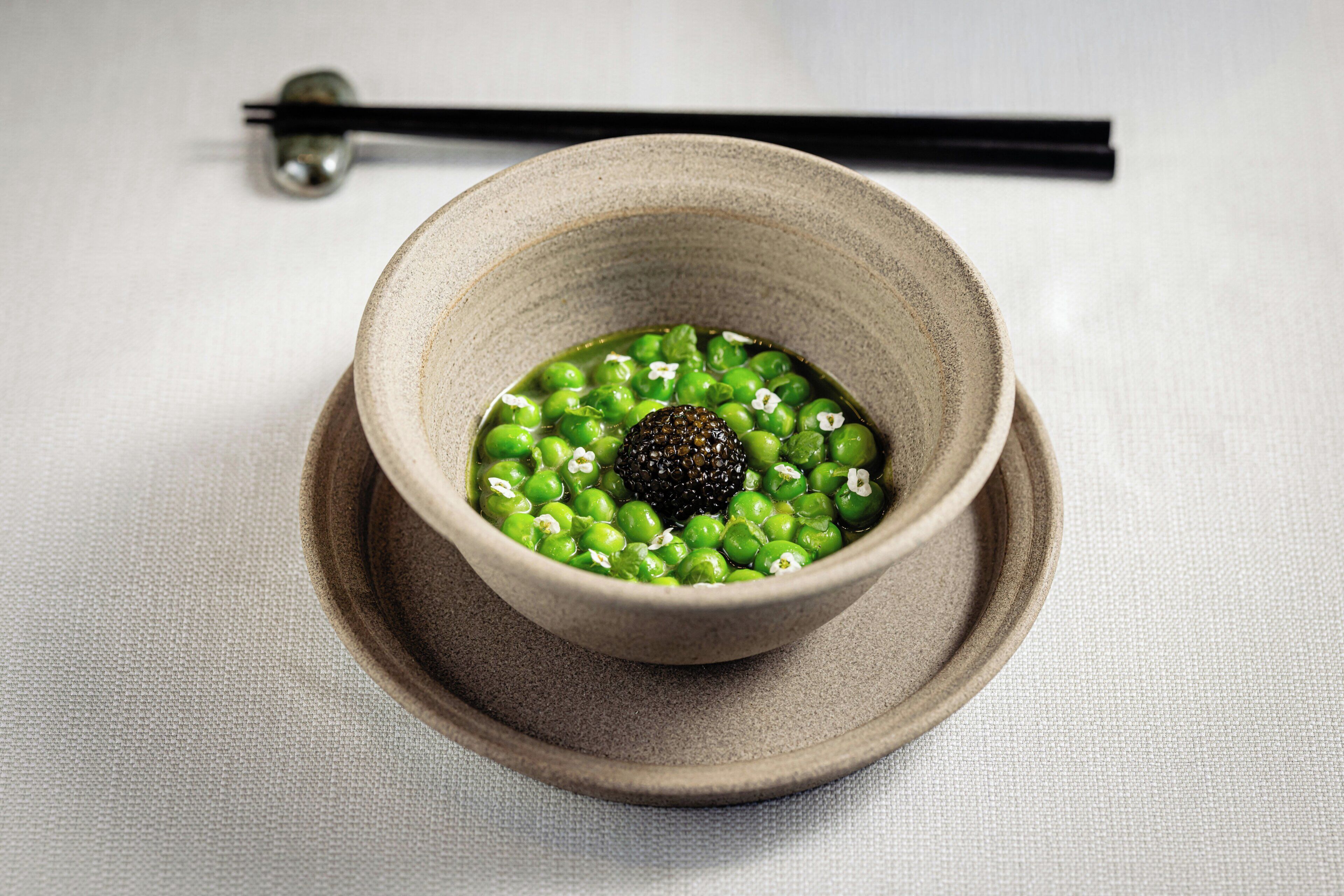 Una ciotola di crema di piselli verdi con un'oliva nera su un piatto di ceramica, servita con bacchette.