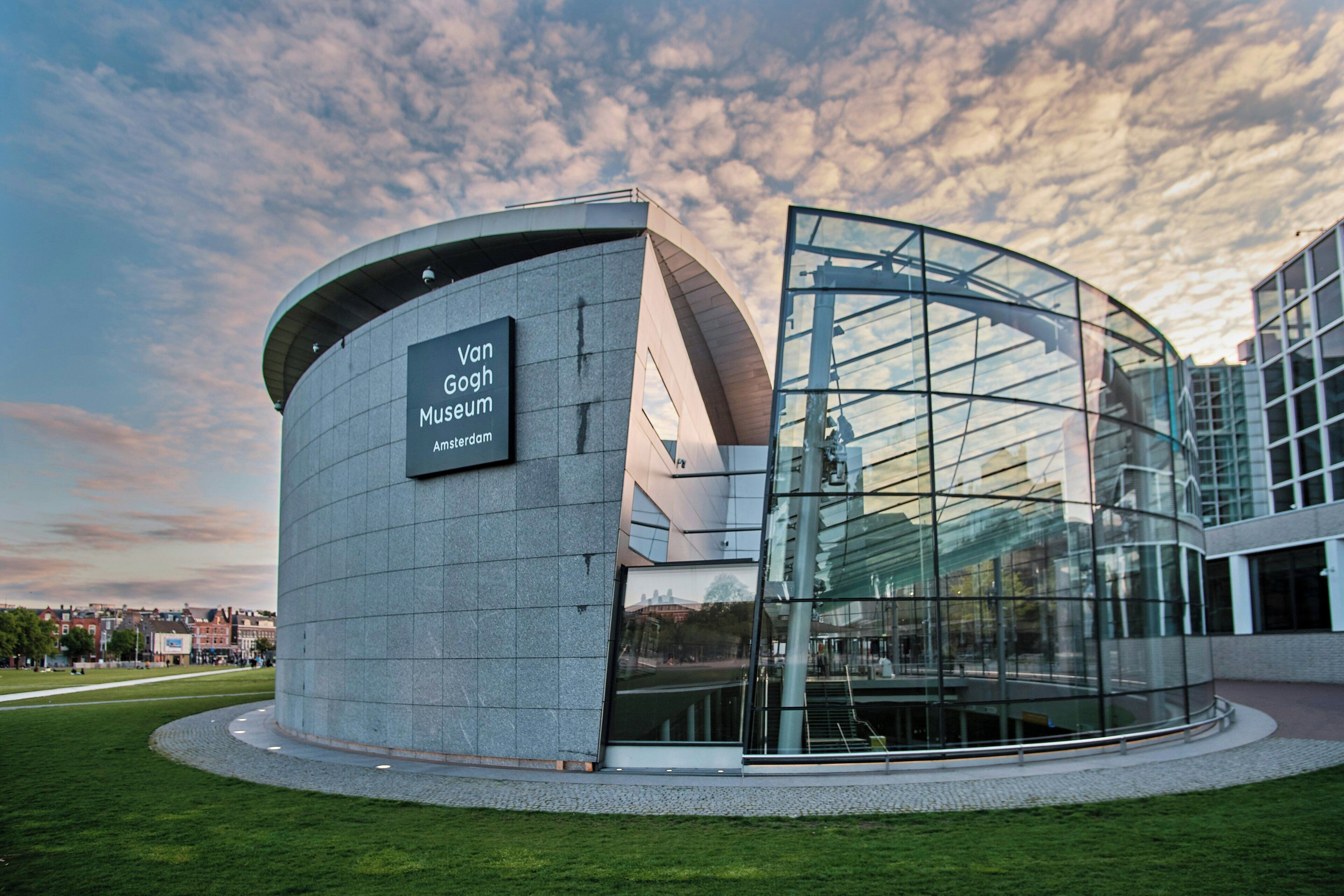 A modern building with a curved glass facade and a sign reading 'Van Gogh Museum Amsterdam.'