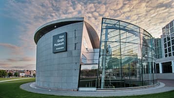 A modern building with a curved glass facade and a sign reading 'Van Gogh Museum Amsterdam.'